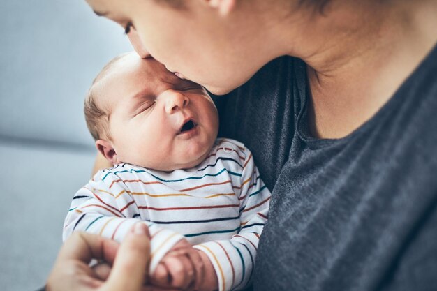 Close-up d'une femme embrassant son fils nouveau-né alors qu'elle est assise sur le canapé à la maison