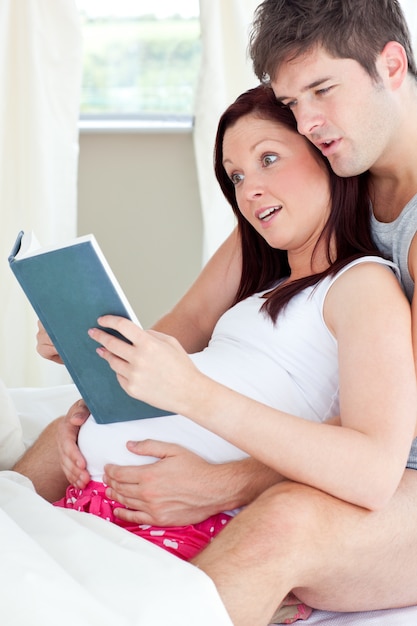 Close-up d&#39;une femme enceinte choquée et son mari lisant un livre sur le canapé à la maison