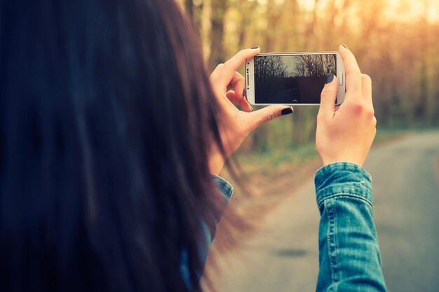 Photo close-up d'une femme photographiant une forêt avec un téléphone portable au coucher du soleil