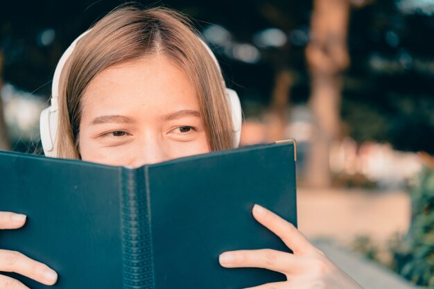 Close-up d'une femme portant des écouteurs qui détourne le regard tout en tenant un livre à l'extérieur