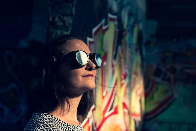 Close-up d'une femme portant des lunettes de soleil par le mur
