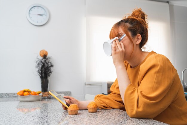 Photo close-up d'une femme prenant un petit déjeuner au thé dans la cuisine à la maison tout en regardant son smartphone