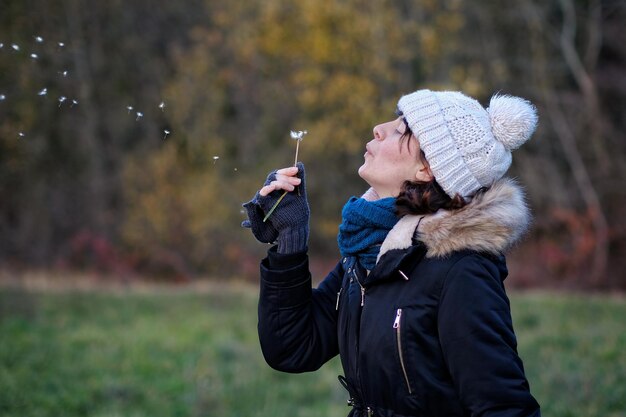 Photo close-up d'une femme secrète soufflant du pissenlit à l'extérieur