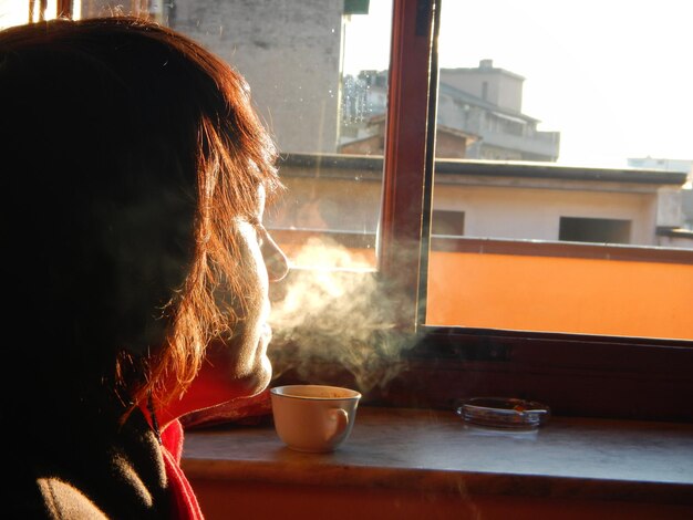 Photo close-up d'une femme avec un verre contre la fenêtre