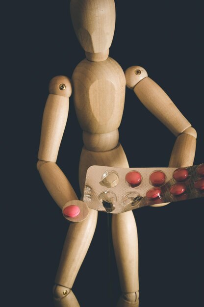 Photo close-up d'une figurine en bois avec des pilules sur fond blanc