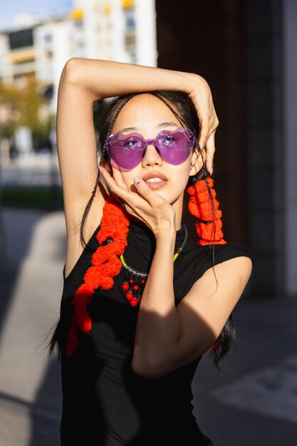 Close-up d'une fille asiatique avec des lunettes de couleur encadrant son visage avec ses mains