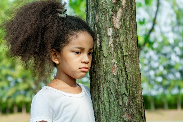 Photo close-up d'une fille triste debout près du tronc d'un arbre dans le parc