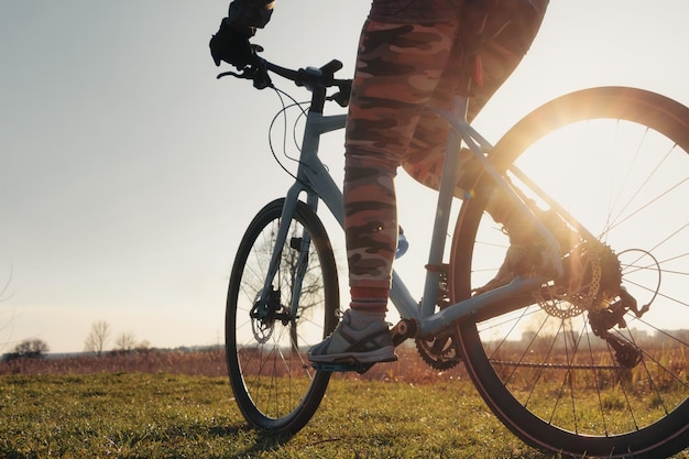 Close-up d'une fille sur un vélo sur l'herbe verte contre le soleil couchant à l'arrière-plan Sport mode de vie entraînement cycliste