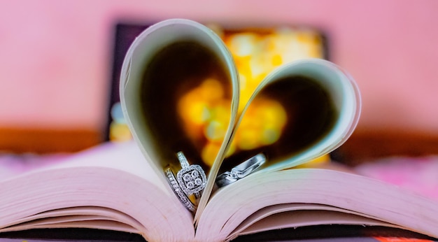 Close-up de la forme d'un cœur sur un livre avec des bagues de fiançailles