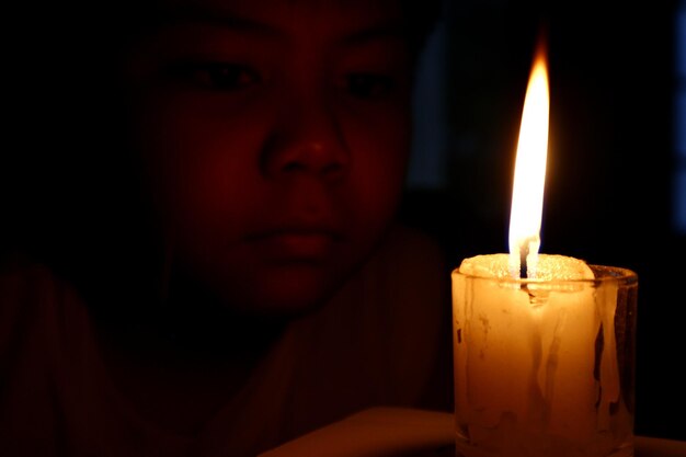 Photo close-up d'un garçon regardant une bougie allumée dans une chambre noire