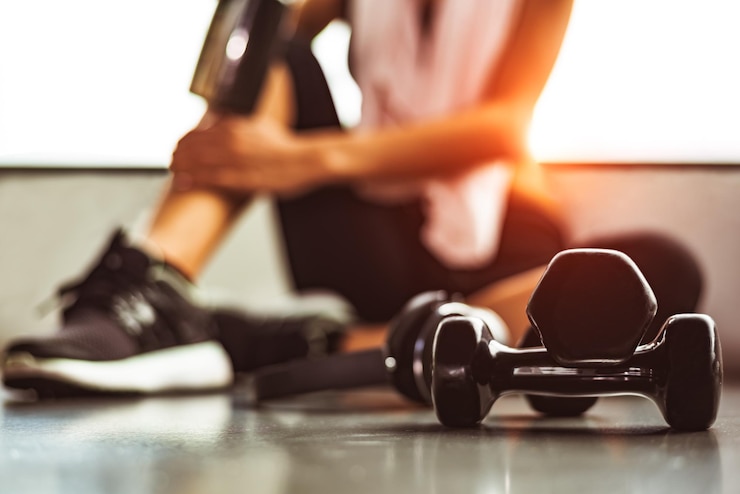 Photo close-up d'un haltère avec une femme assise sur le sol dans le gymnase