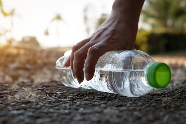 Close up Hand ramasser une bouteille d'eau en plastique transparent avec une casquette verte sur la route dans le parc