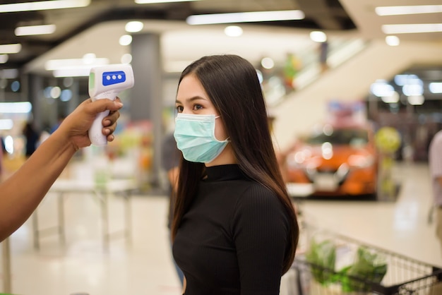 Close up hand Utilisation d'un pistolet à température avec une jeune femme, mesure de distanciation sociale pour la prévention du COVID-19 dans un centre commercial