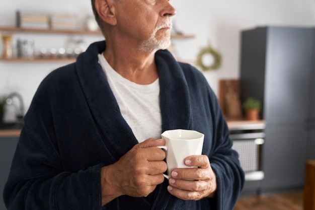 Close-up d'un homme âgé tenant une tasse de café à la maison