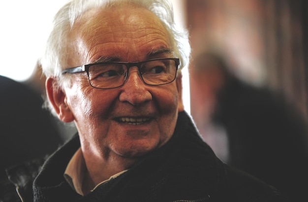 Close-up d'un homme mature portant des lunettes regardant ailleurs alors qu'il est assis à l'intérieur