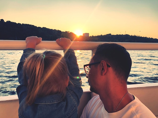 Close-up d'un homme avec sa fille sur un bateau dans un lac contre un ciel clair au coucher du soleil