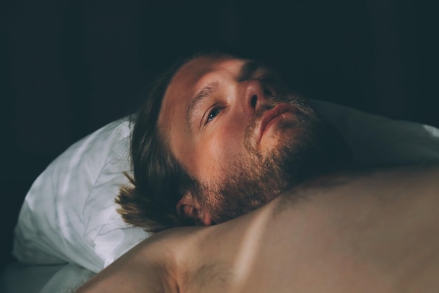 Close-up d'un homme sans chemise réfléchi détournant le regard alors qu'il est allongé sur le lit