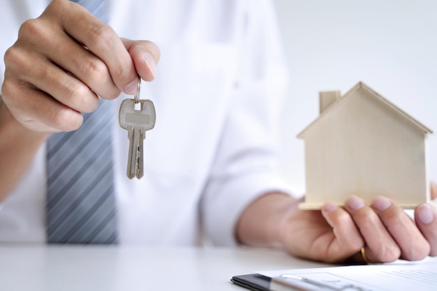 Close-up d'un homme tenant des clés avec une maison modèle sur la table