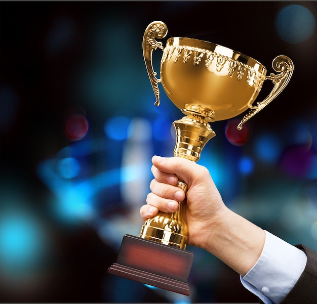 Close-up human hand holding golden Trophy sur fond bleu flou