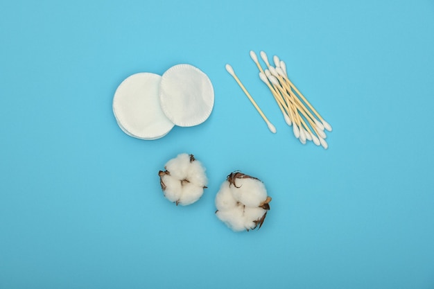 Close up hygiène féminine et soins de beauté à plat d'éponges de maquillage, de tampons d'oreille et de fleurs de coton sur fond bleu, vue de dessus élevée, directement au-dessus