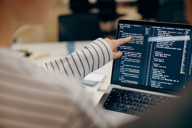 Close-up d'une ingénieure en logiciel écrivant du code sur un ordinateur portable avec des écrans configurés dans un coworking