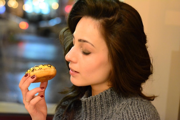 Close-up d'une jeune femme mangeant un beignet près de la fenêtre