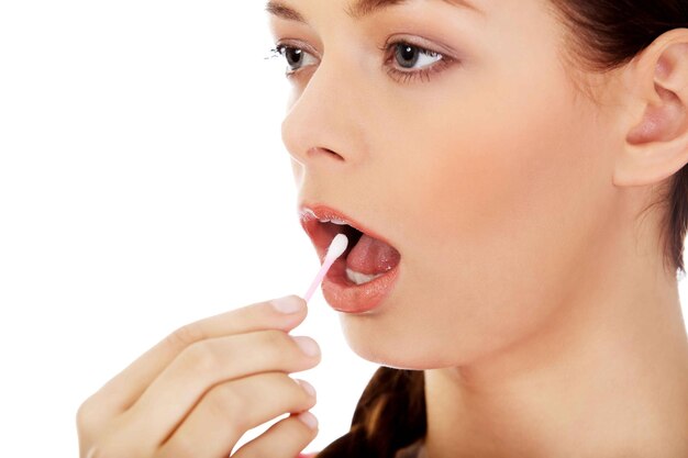 Close-up d'une jeune femme mettant un coton-tige dans la bouche sur un fond blanc