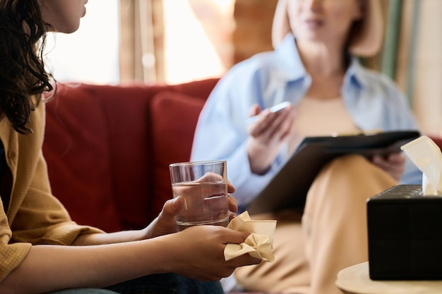 Close-up d'une jeune femme avec un mouchoir et un verre d'eau parlant de ses problèmes à un psychologue