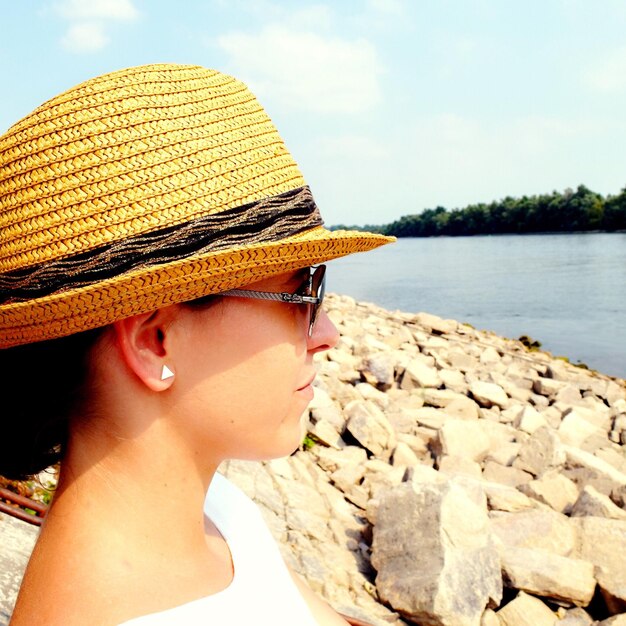 Photo close-up d'une jeune femme réfléchie portant un chapeau debout contre la rivière