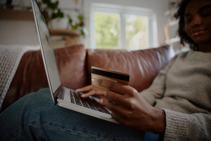 Photo close-up d'une jeune femme tenant une carte de débit bancaire en faisant un paiement sur un ordinateur portable à la maison