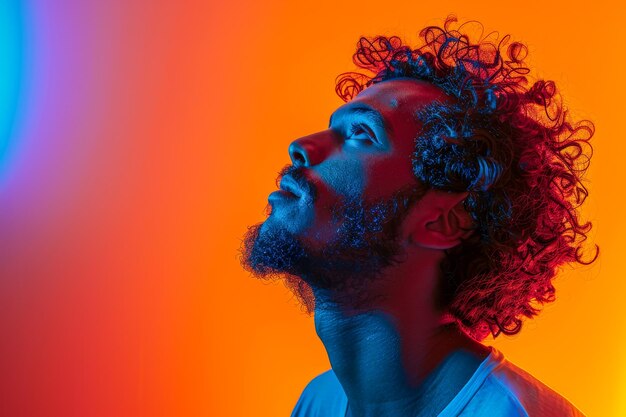 Close-up d'un jeune homme avec une barbe baigné dans une lumière bleue et rouge spectaculaire lui donnant une apparence contemplative et d'humeur