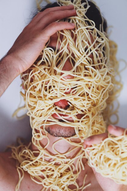 Photo close-up d'un jeune homme couvert de spaghettis contre le mur