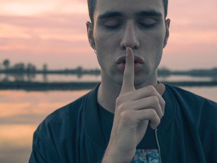 Photo close-up d'un jeune homme avec un doigt sur les lèvres près du lac au coucher du soleil