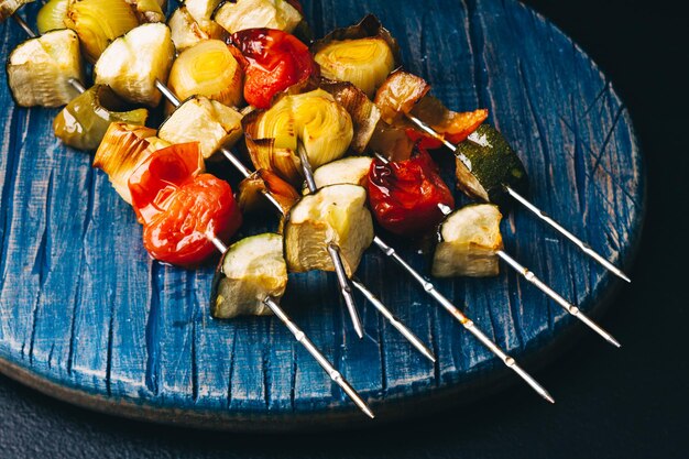 Close up de légumes grillés sur des brochettes métalliques sur la planche de bois