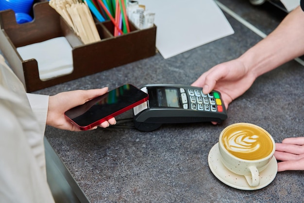 Close-up d'une main de client avec un smartphone payant pour une tasse de café