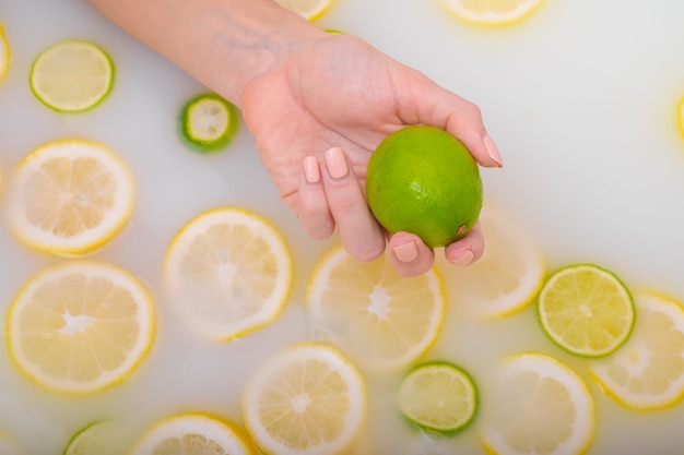Photo close-up d'une main féminine tenant un citron vert sur de l'eau blanche avec des tranches de citron