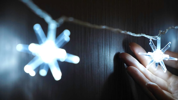 Close-up de la main de la femme touchant la belle guirlande de Noël électrique de lumières brillantes suspendues