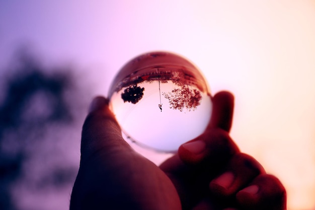 Photo close-up de la main tenant une boule de cristal contre les arbres pendant le coucher du soleil