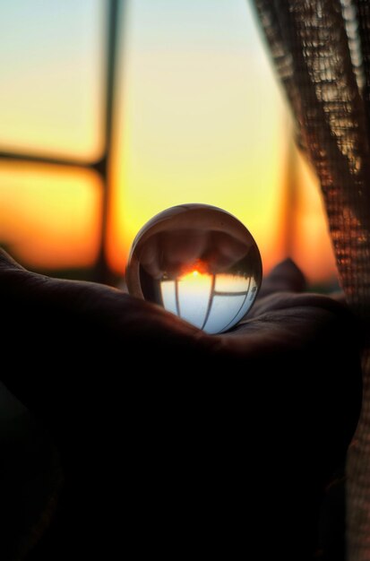 Close-up de la main tenant une boule de cristal contre la fenêtre