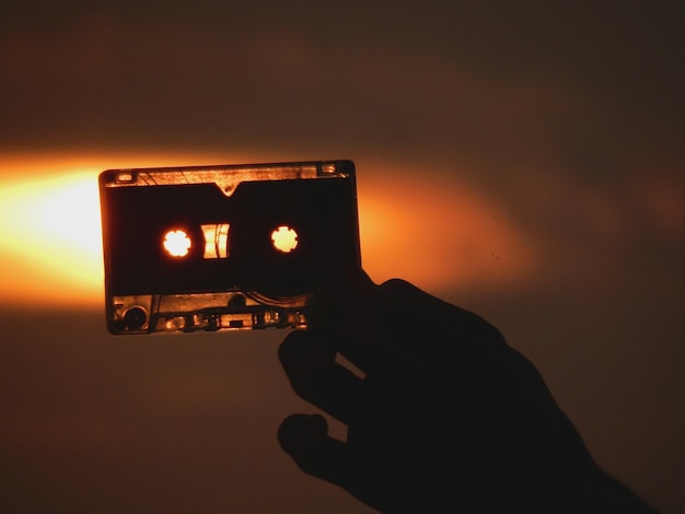 Close-up d'une main tenant une cassette audio contre le ciel au coucher du soleil