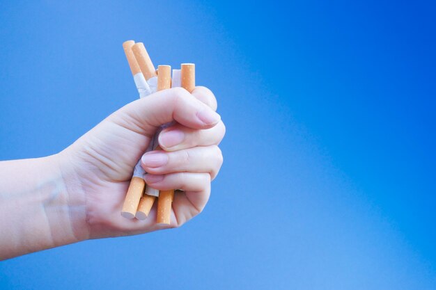 Close-up d'une main tenant des cigarettes sur un fond bleu