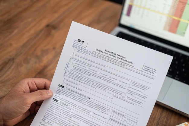 Close-up d'une main tenant un formulaire d'impôt w9 avec un ordinateur portable en arrière-plan la préparation de l'impôt et