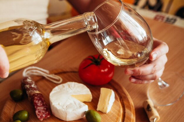 Photo close-up de la main versant du vin dans un verre à vin avec de la nourriture sur une planche à couper