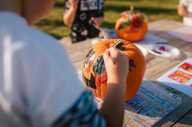 Photo close-up des mains d'un enfant en train de peindre une citrouille pour halloween