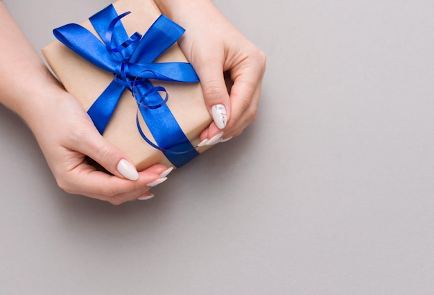 Close-up de mains de femmes tenant une boîte à cadeaux sur un fond gris
