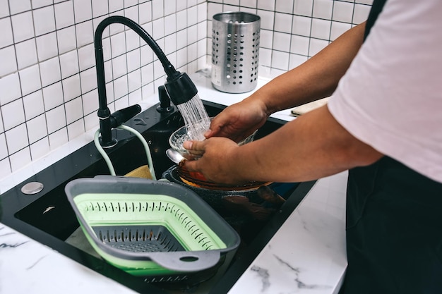 Close up des mains lavant la vaisselle sale avec une éponge à mousse de savon dans l'évier de la cuisine