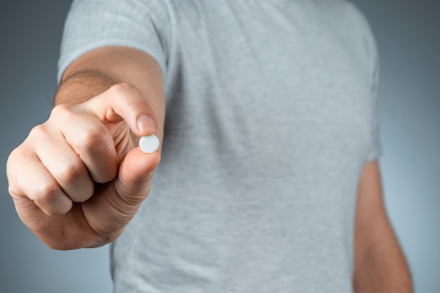 Close-up male hands holding a white pill, prenant des médicaments, traitement, mur gris. Thème médical, vitamines, soins de santé.