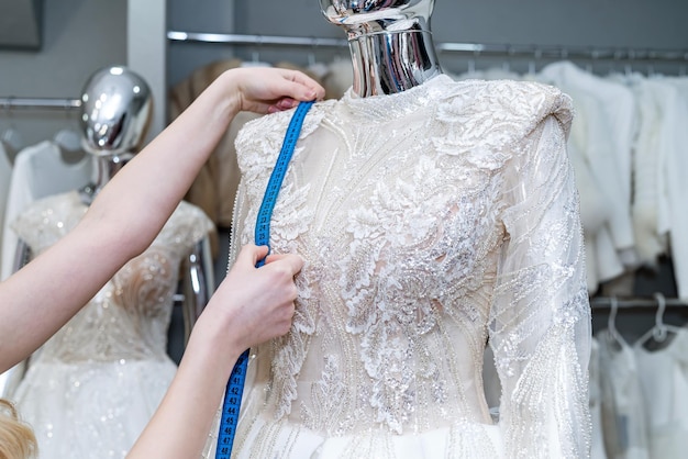 Close up of female designer couturière raccord à la main robe de mariée avec ruban à mesurer en boutique