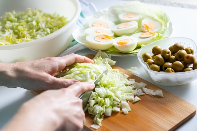 Close up of female hands tranchage salade verte sur planche de bois sur un fond de tableau blanc