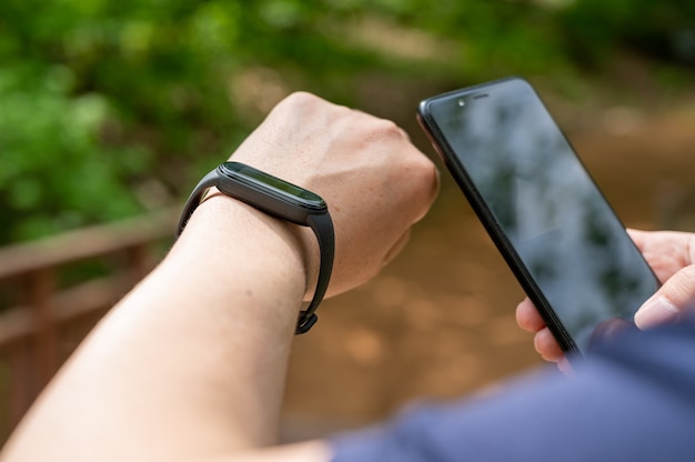 Close-up of male hands holding smartwatch et smartphone sur la promenade